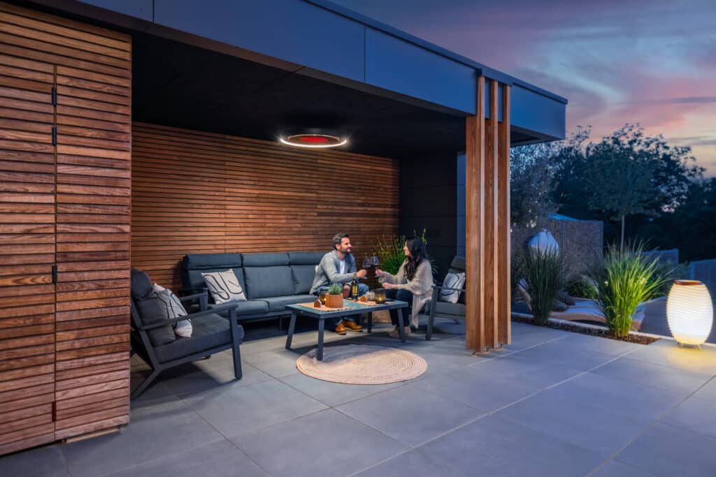 Two people sitting on a patio with outdoor furniture and lighting.