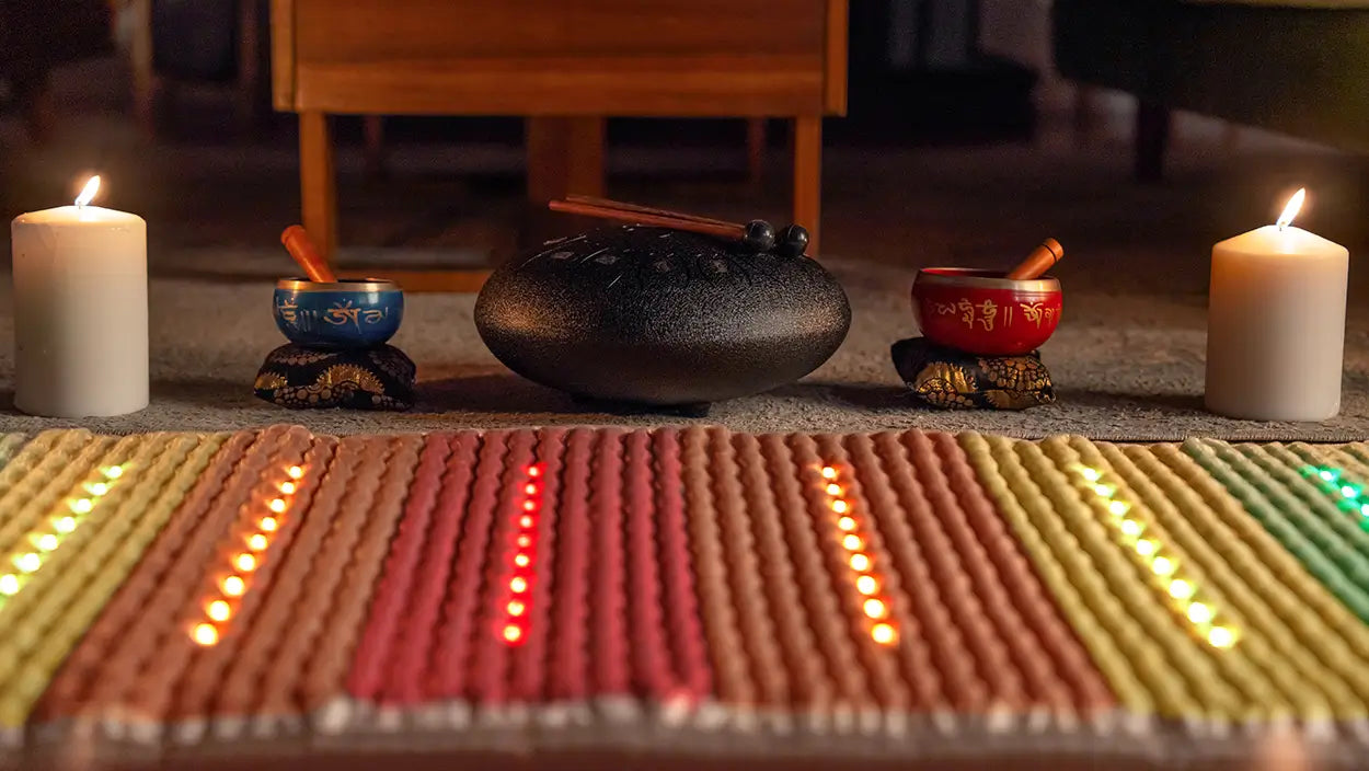 Ceremonial setup with candles, bowls, and a stone on a mat.