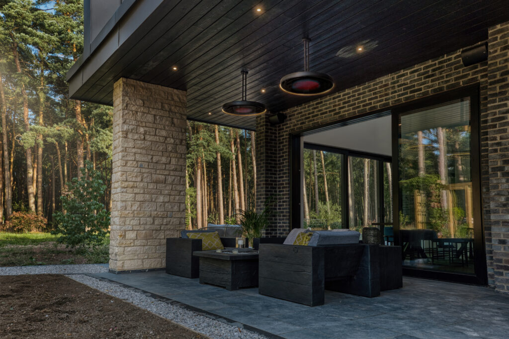 Modern outdoor patio area with furniture and large windows overlooking a forest.