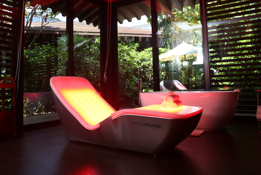 EnergyLounger red and near-infrared therapy lounger glowing in an outdoor-style wellness retreat.