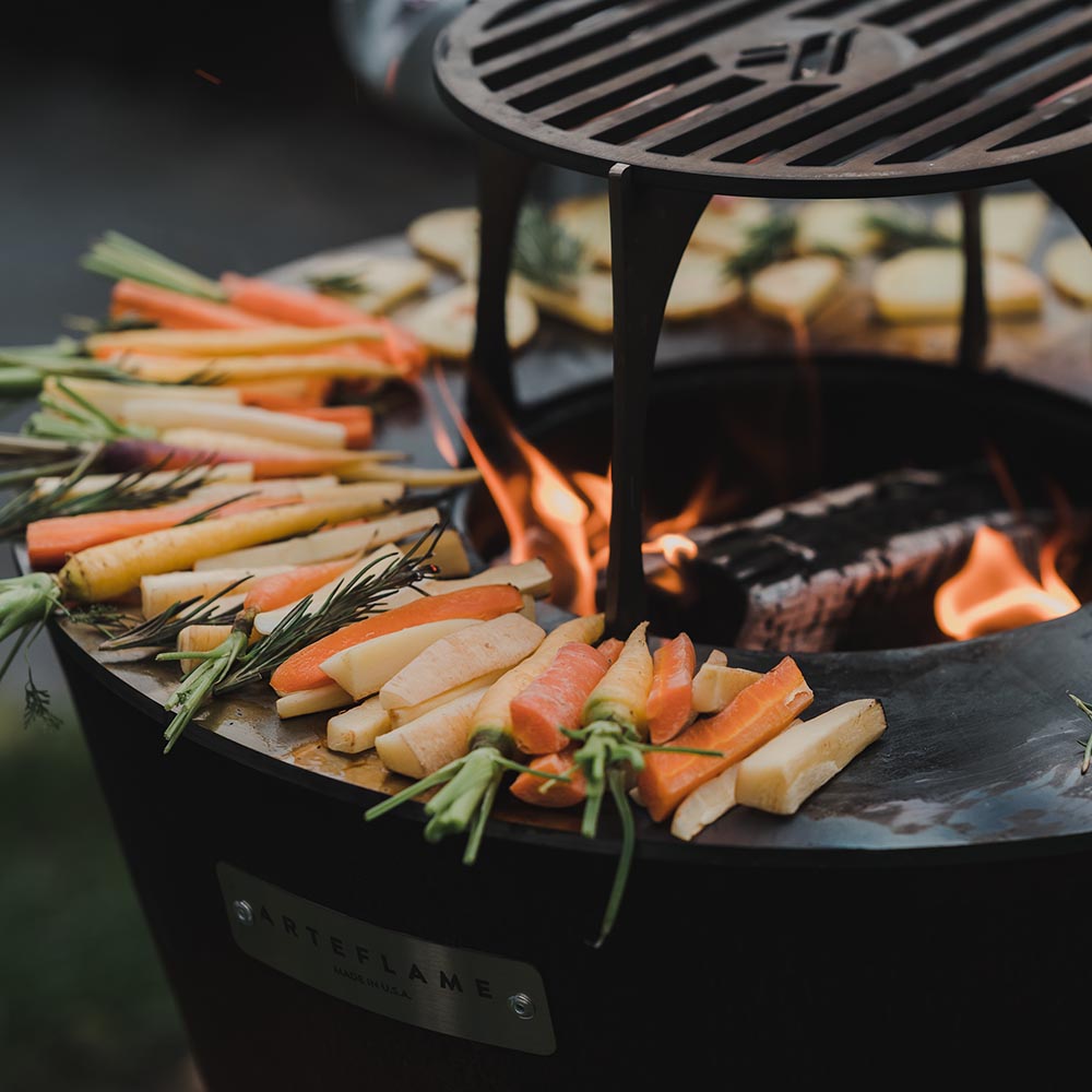Close-up of vegetables and meat searing on the Arteflame flat-top cooking surface over an open flame.