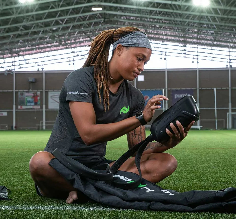 Athlete using Rapid Reboot REGEN boots while trainer adjusts settings on the control unit.