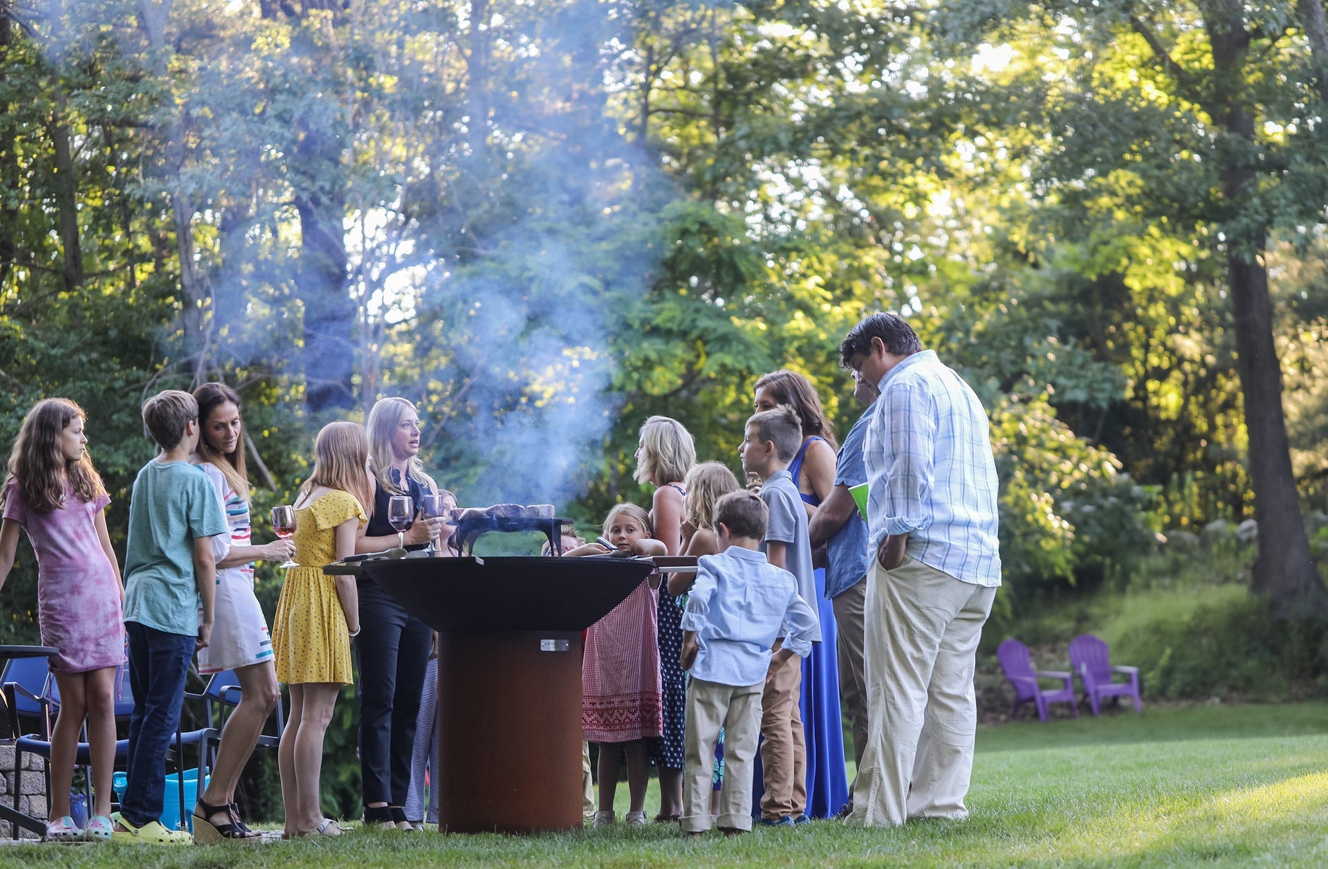 Group of people enjoying a backyard cookout around the Arteflame Classic 40-inch Corten steel grill.